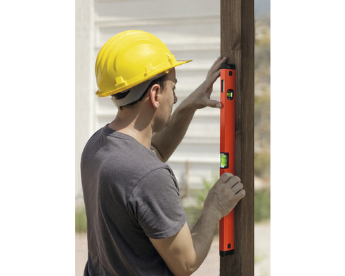 Muž s ochrannou prilbou a vodováhou na drevenom stĺpiku