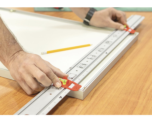 Remeselník používa meraciu tyč s vodováhou na vyrovnanie rámu obrazu.