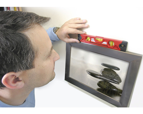 Osoba vyrovnáva zarámovaný obraz pomocou vodováhy.