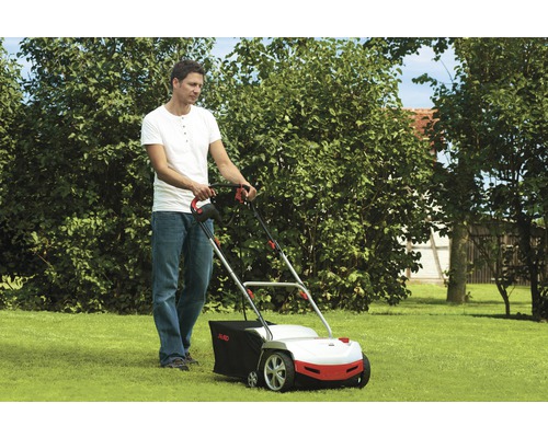 Muž používa vertikutátor na záhrade.