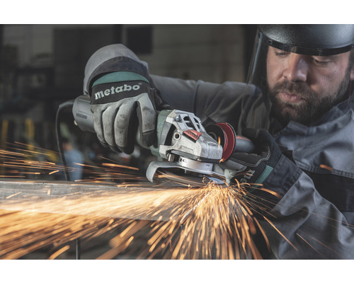 Muž brúsi kov uhlovou brúskou, z ktorej lietajú iskry. Má na sebe rukavice a ochranné okuliare.