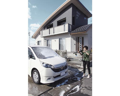 Žena čistí auto vysokotlakovým čističom pred domom.