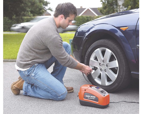Muž hustí pneumatiku automobilu pomocou prenosného kompresora