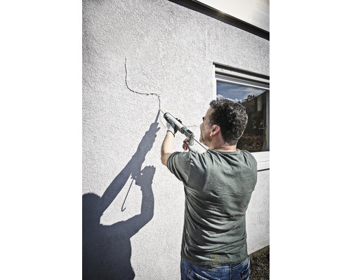 Muž utesňuje trhlinu v stene tesniacou pištoľou.