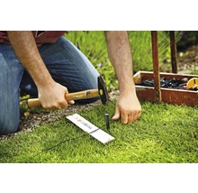 Osoba zatĺka kolík kladivom do zeme na upevnenie systému Gardena Micro-Drip.