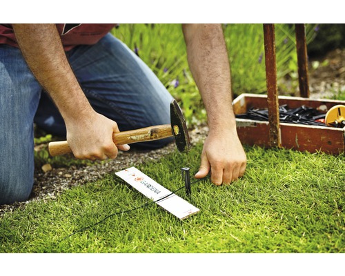Osoba zatĺka držiak rúrky systému Gardena Micro-Drip do trávnika