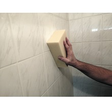 Ruka drží špongiu na obkladanej stene.