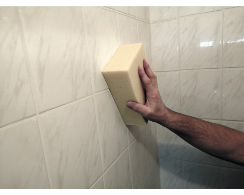 Ruka drží špongiu na obkladanej stene.