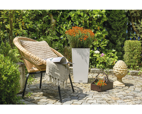 Záhradná scéna s prúteným kreslom, kvetináčom a dekoráciou na kamennej podlahe