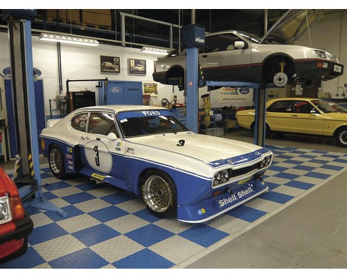 Scéna dielne s niekoľkými veteránmi, vrátane vozidla Ford Capri s modrými akcentmi a číslom tri.