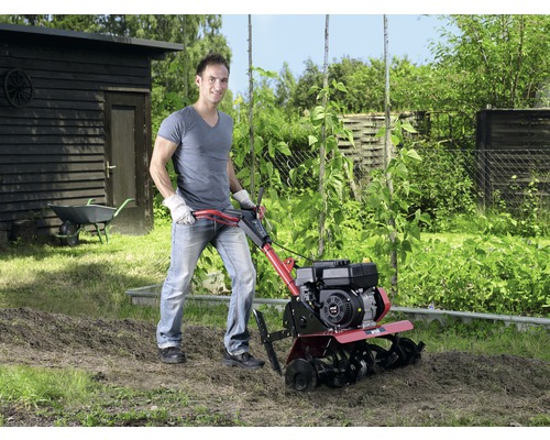 Muž pracuje s motorovým kultivátorom v záhrade na spracovanie pôdy.