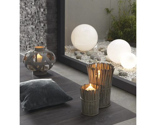 Dekoratívna scéna s lampášom, vankúšom, veternými svetlami z konárov a záhradnými guľami na štrku