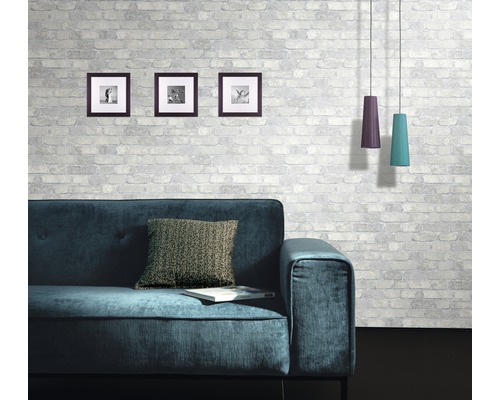 Obývacia izba s pohovkou, vankúšom, obrazmi a závesnými svietidlami pred murovanou stenou so vzorom