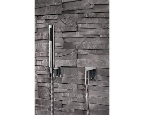 Ručná sprcha so sprchovou hadicou pred kamennou stenou