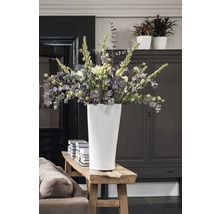 Vysoká biela váza s kyticou na drevenej lavici v izbe