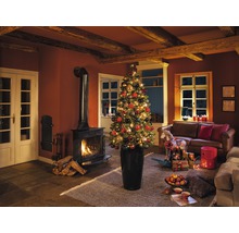 Vianočná obývacia izba s krbom, gaučom a ozdobeným vianočným stromčekom v kvetináči.