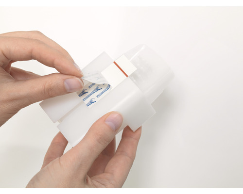 Osoba odstraňuje ochrannú fóliu z upevňovacieho prúžku na zariadení.