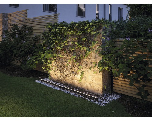 Osvetlená záhradná stena s porastom a trávnikom.