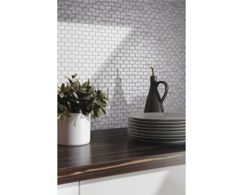 Kuchynská scéna s obkladmi s tehlovým vzhľadom, rastlinou, taniermi a fľašou oleja na tmavej pracovnej doske.