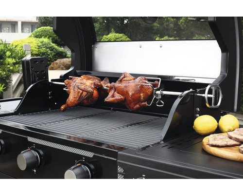 Plynový gril s dvoma pečenými kurčatami na otočnom ražni a citrónmi na drevenej doske