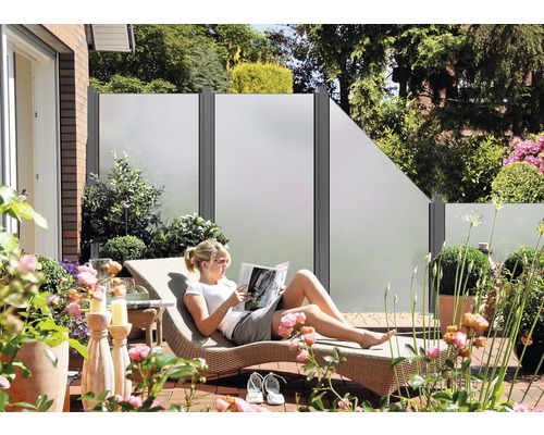 Terasa s prvkami na ochranu súkromia, záhradným nábytkom a ženou na lehátku