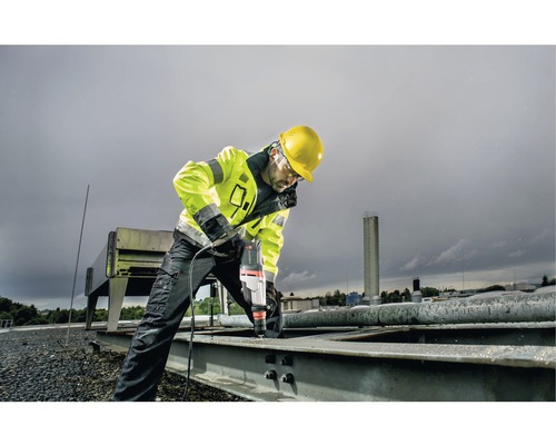 Stavebný robotník vŕta vŕtačkou dieru do kovového dielu na streche.