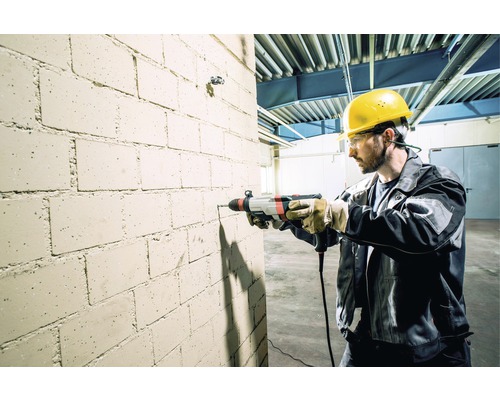 Muž vŕta do tehlovej steny s vŕtacím kladivom.