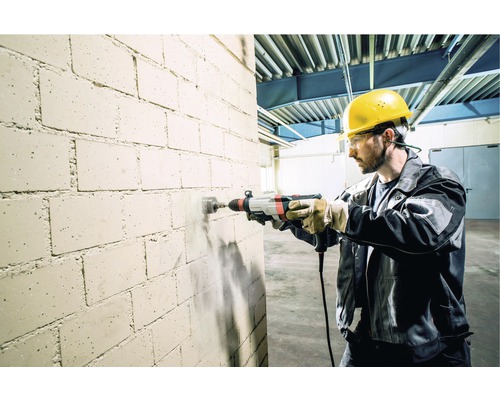 Muž vŕta dieru do tehlovej steny príklepovou vŕtačkou.