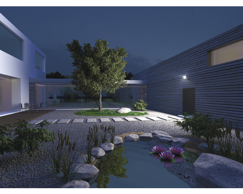 Osvetlená záhrada s jazierkom, kameňmi, rastlinami a moderným domom v noci