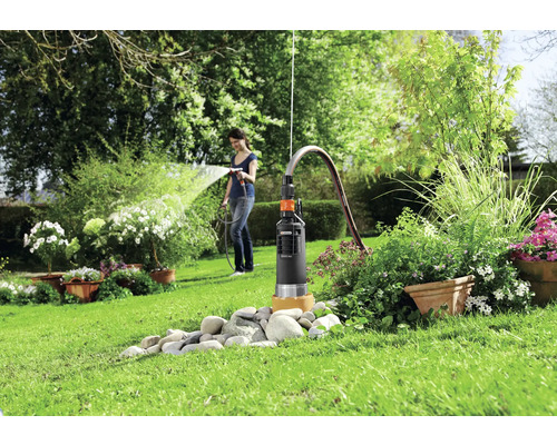 Záhrada s hlbinným čerpadlom a ženou zalievajúcou rastliny