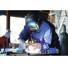 Zvárač so zváračskou helmou a rukavicami pracuje s kovom.