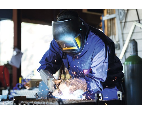 Zvárač so zváračskou helmou a rukavicami pracuje s kovom.