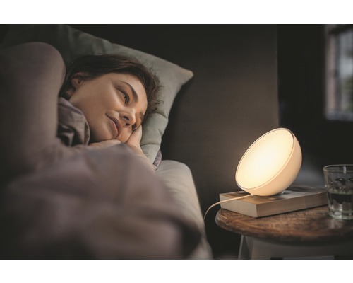 Žena leží v posteli vedľa nočnej lampy.