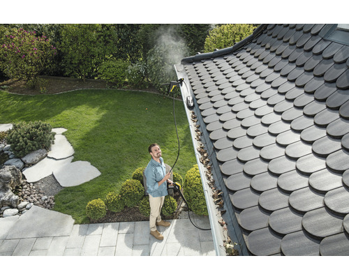 Muž čistí odkvap pomocou tlakovej umývačky v záhrade.