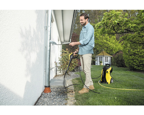 Muž čistí odkvap pomocou vysokotlakového čističa Kärcher v záhrade.