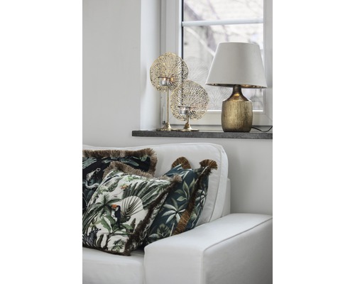 Dekoratívna obývacia izba s pohovkou, vankúše s motívmi džungle, stolná lampa a držiaky na čajové sviečky