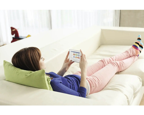 Žena ovláda kúrenie pomocou tabletu inteligentnej domácnosti na pohovke