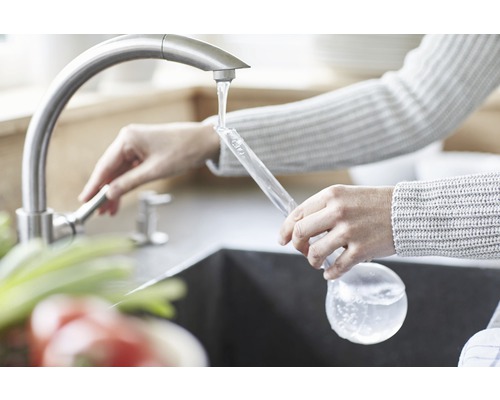 Žena plní sklenenú fľašu vodou z vodovodu