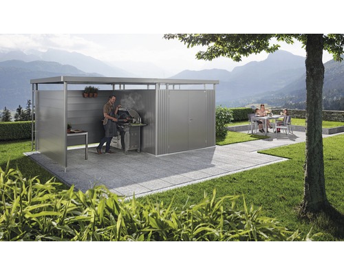 Zastrešené grilovacie miesto s mužom grilujúcim a rodinou v pozadí