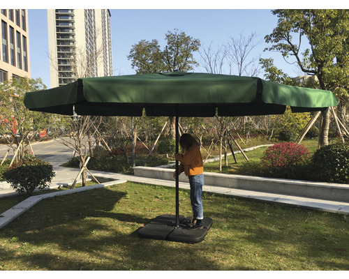 Osoba stavia veľký slnečník s obdĺžnikovým tienidlom na trávniku.