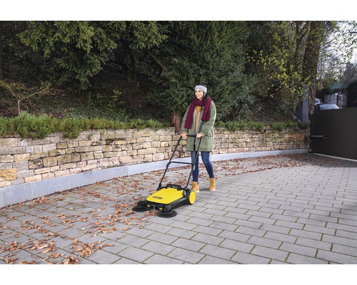 Žena používa žltý zametací stroj na odstraňovanie lístia z príjazdovej cesty.