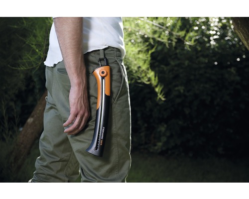 Muž s ručnou pílou Fiskars v upevnení nohavíc v záhrade