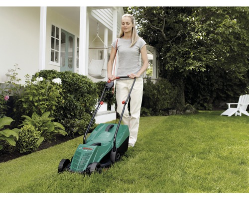 Žena obsluhuje kosačku na trávu v záhrade.