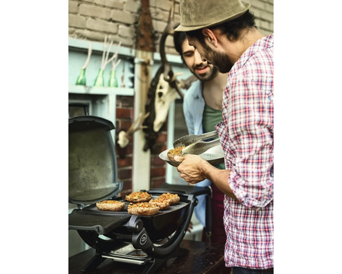 Dvaja muži grilujú plnené šampiňóny na guľovom grile vonku.