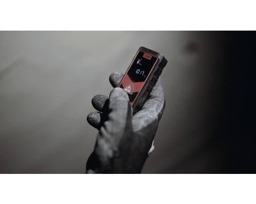 Ruka s pracovnou rukavicou drží laserový diaľkomer.