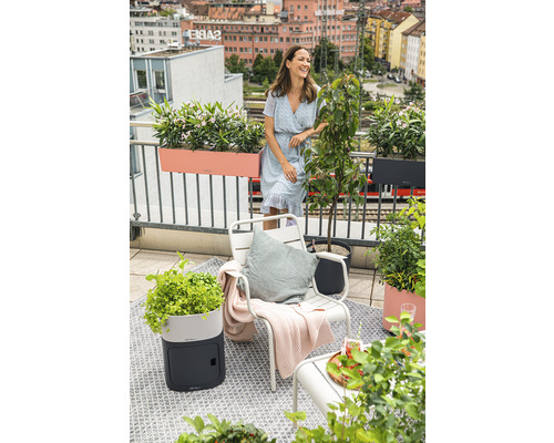 Balkónová scéna so ženou, stoličkou, kvetináčmi a výhľadom na mesto