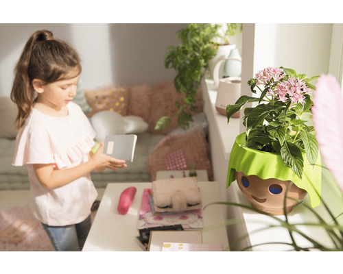 Dievča s poznámkovým blokom vedľa kvetináča s dizajnom tváre v detskej izbe.