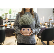 Žena drží kvetináč v tvare štylizovanej hlavy s rastlinou