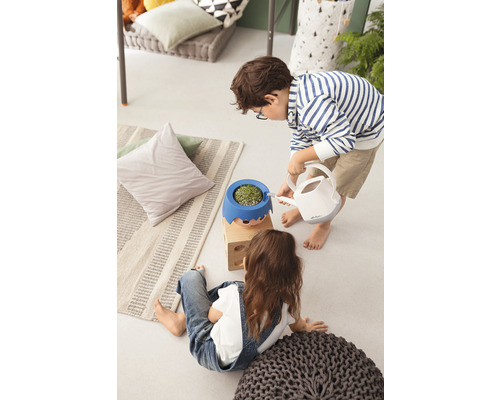 Dve deti v interiéri, jedno zalieva rastlinu v kvetináči s tvárou kanvou.