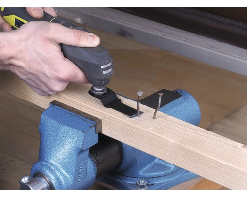 Osoba používa multifunkčný nástroj na rezanie klincov v drevenej doske, ktorá je upevnená vo zveráku.